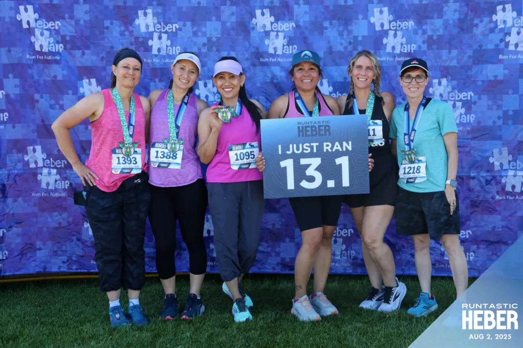 Runtastic HEBER Finishers in Heber City, Utah Six smiling Runtastic HEBER female finishers with medals, holding up an "I just ran 13.1" sign in front of a blue photo backdrop